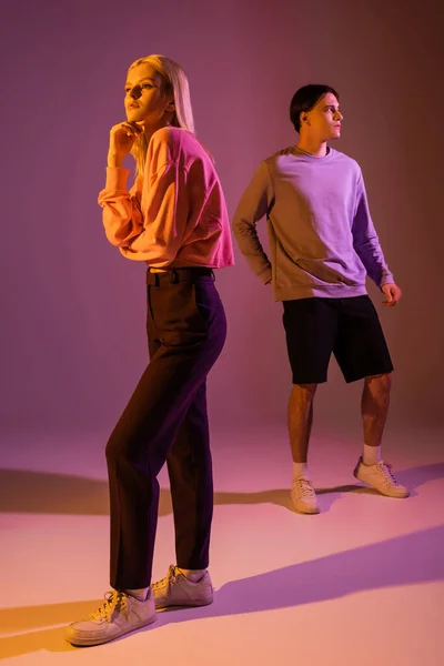 Full length of pretty blonde woman posing near boyfriend on purple background with lighting — Stock Photo