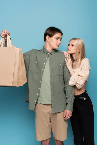 Jovem casal elegante com sacos de compras olhando uns para os outros no fundo azul — Fotografia de Stock