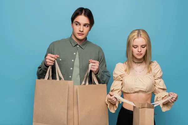 Jeune couple branché tenant des sacs à provisions isolés sur bleu — Photo de stock