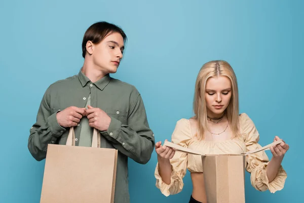 Pretty blonde woman looking at shopping bag near boyfriend isolated on blue — Fotografia de Stock