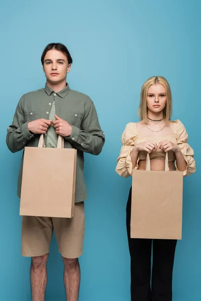 Trendy young woman holding shopping bags and looking at camera isolated on blue — Stock Photo