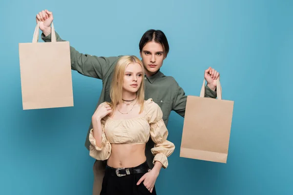 Elegante uomo che tiene borse della spesa vicino alla ragazza su sfondo blu — Foto stock