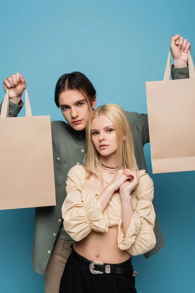 Stylish couple posing with shopping bags on blue background — Stock Photo
