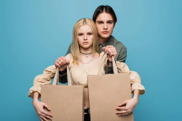 Jovem casal na moda posando com compras isoladas em azul — Fotografia de Stock