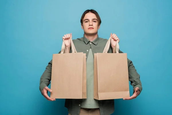 Mujer sosteniendo bolsas de compras cerca de novio con estilo sobre fondo azul - foto de stock