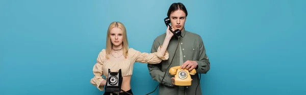 Trendy young woman holding handset near boyfriend isolated on blue, banner — Stock Photo