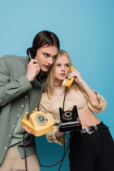 Fashionable couple talking on retro telephones on blue background — Stockfoto