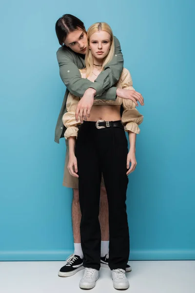 Full length of young man embracing girlfriend on blue background — Fotografia de Stock