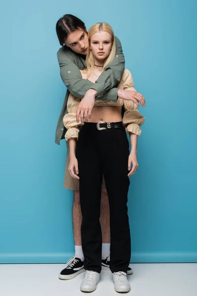 Full length of young man embracing girlfriend on blue background — Stock Photo