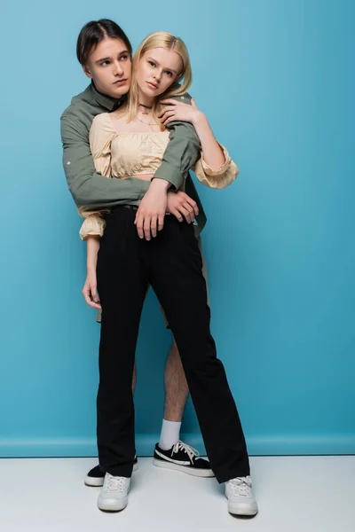 Full length of young man embracing stylish girlfriend on blue background — Foto stock