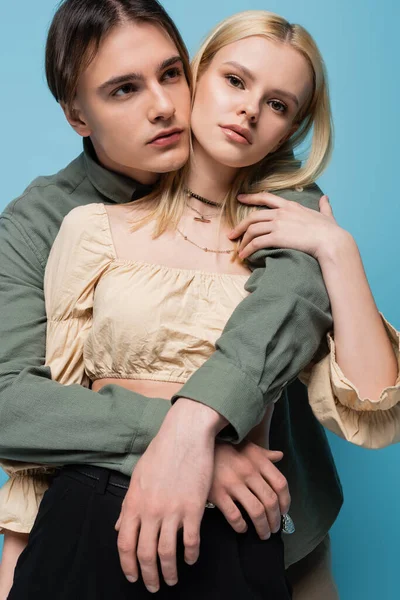 Low angle view of brunette man embracing blonde girlfriend in blouse isolated on blue - foto de stock