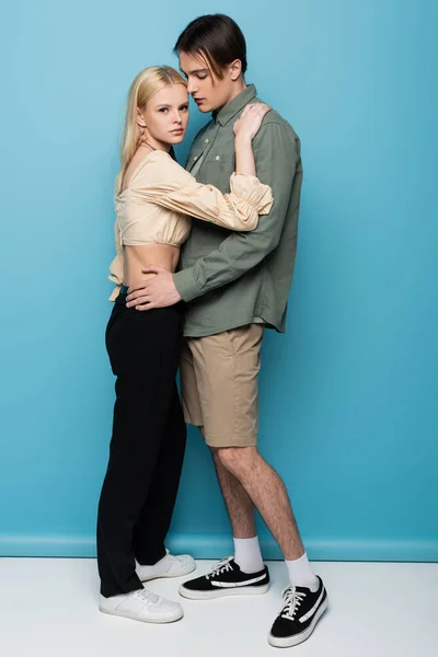 Full length of trendy young couple hugging on blue background - foto de stock