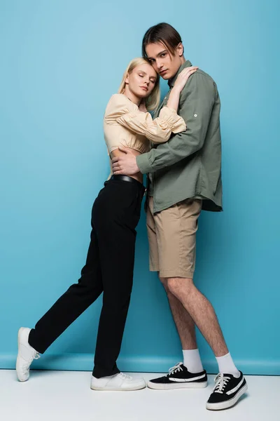 Stylish man in shirt hugging blonde girlfriend on blue background — Stockfoto