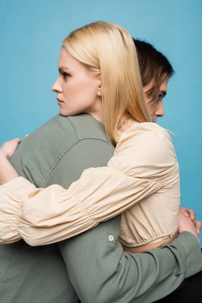 Vista laterale della giovane coppia che abbraccia isolato sul blu — Foto stock