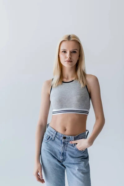 Pretty blonde woman in jeans and top standing isolated on grey — Stock Photo