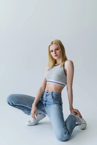 Jeune femme tendance en haut et jeans posant sur fond gris — Photo de stock
