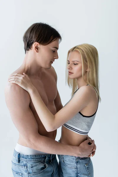 Young woman in top and jeans hugging shirtless boyfriend isolated on grey - foto de stock