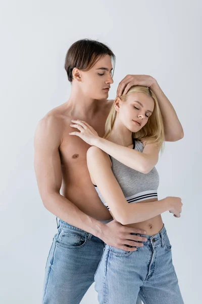 Musculoso hombre en jeans tocando bonita novia aislada en gris - foto de stock