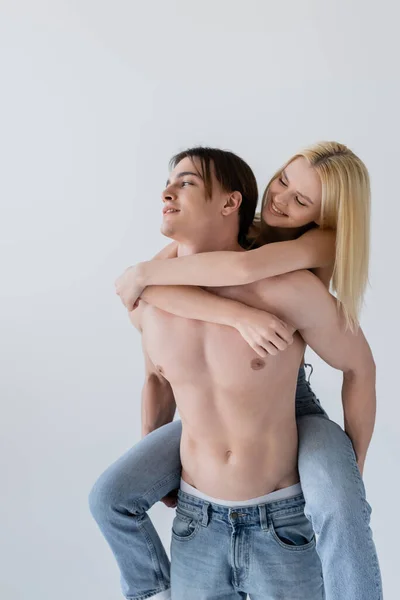 Mujer rubia sonriente abrazando novio sin camisa en jeans aislados en gris — Stock Photo