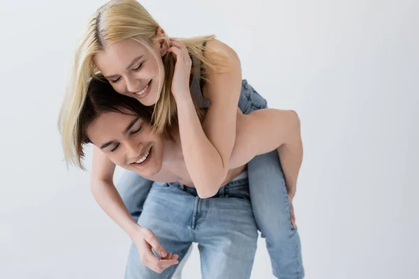 Feliz rubia mujer piggybacking en sin camisa novio aislado en gris - foto de stock