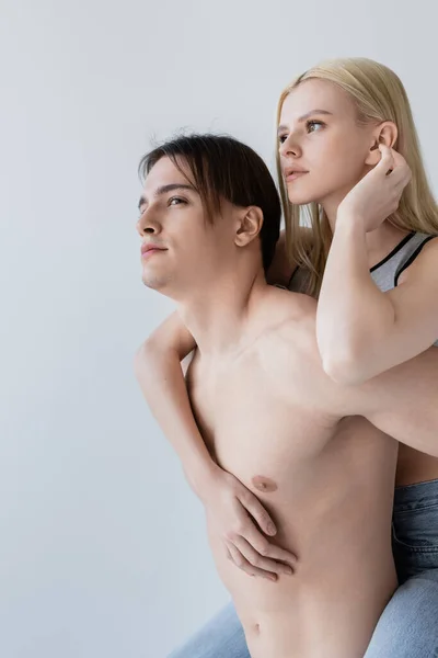 Junge Frau huckepack auf muskulösen Freund isoliert auf grau — Stockfoto