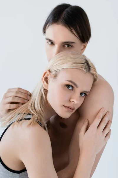 Junge Frau umarmt hemdlosen Freund und blickt isoliert in die Kamera auf grau — Stockfoto