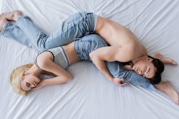 Vista dall'alto della giovane coppia in jeans sdraiati con gli occhi chiusi sul letto — Foto stock