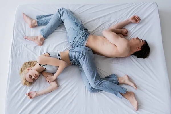 Top view of young couple in jeans lying on bed on grey background — Stock Photo