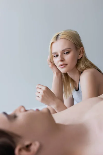 Blonde woman looking a blurred shirtless boyfriend on bed isolated on grey — Photo de stock