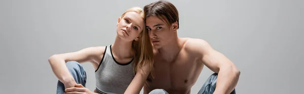 Young woman in top looking at camera near shirtless boyfriend isolated on grey, banner — Stock Photo