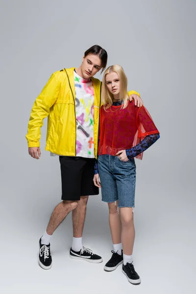 Brunette man in windbreaker hugging blonde girlfriend on grey background — Photo de stock