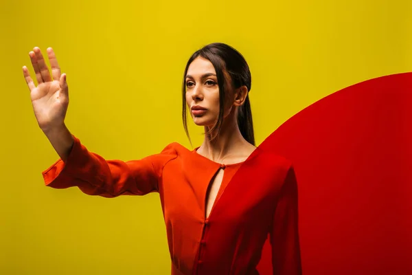 Stylish young woman in red dress showing stop sign near round shape glass isolated on green — Foto stock