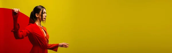 Stylish young woman in red dress holding glass and looking away isolated on green, banner - foto de stock