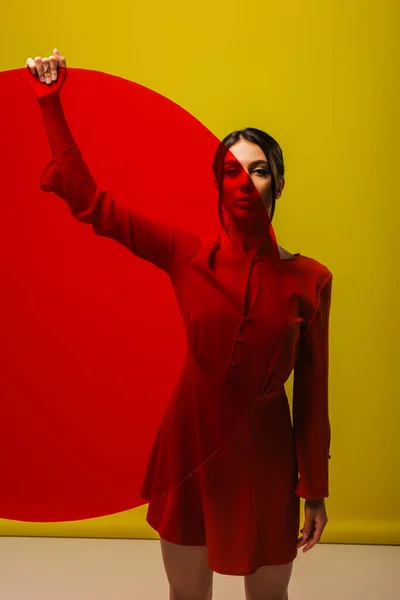 Pretty young woman in red dress holding round shape glass on green — Photo de stock