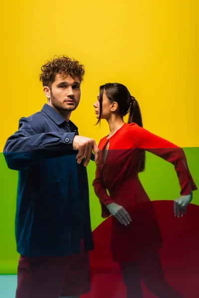 Curly man and stylish woman holding different shapes glass while posing isolated on yellow - foto de stock