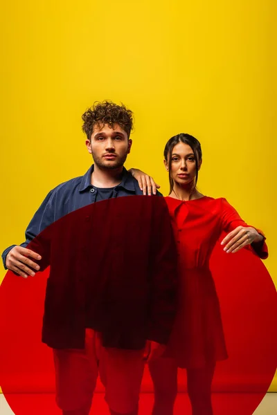 Trendy woman and man holding round shape glass while posing isolated on yellow — Photo de stock