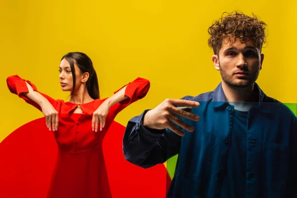 Homem encaracolado e mulher elegante segurando vidro de diferentes formas isoladas no amarelo — Fotografia de Stock