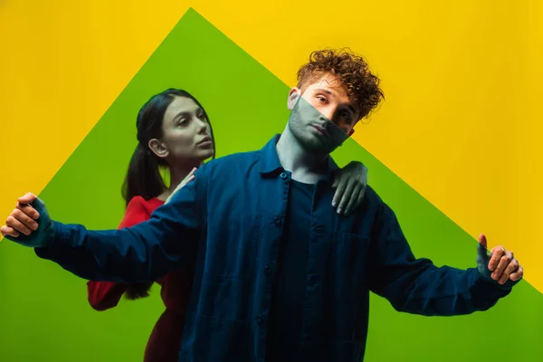 Curly man holding green square shape glass near woman isolated on yellow — Fotografia de Stock