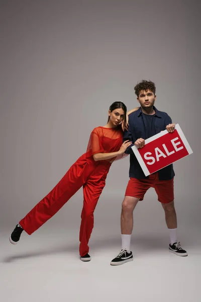 Full length of young couple holding paper with sale lettering on grey — Foto stock