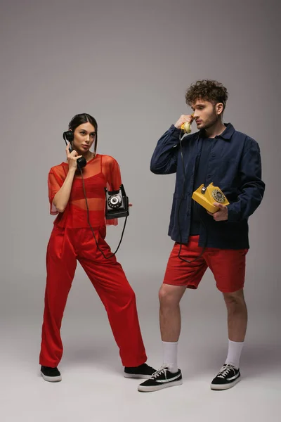 Full length of young woman and curly man holding retro handsets and telephones on grey — Stock Photo