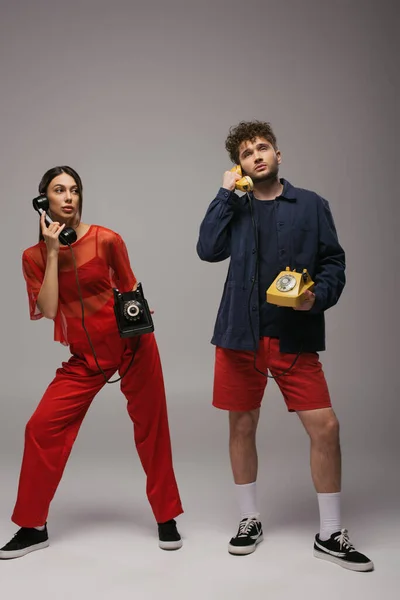 Full length of young models holding handsets and retro telephones on grey — Stockfoto