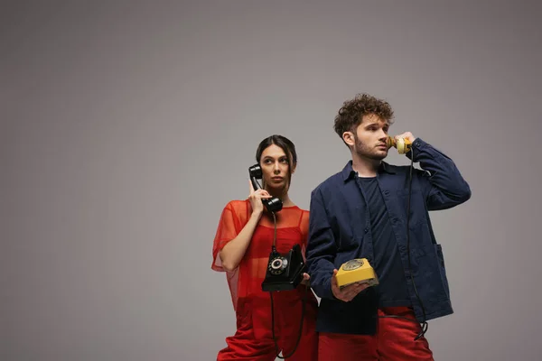 Stylish young couple holding handsets and telephones isolated on grey — Stock Photo