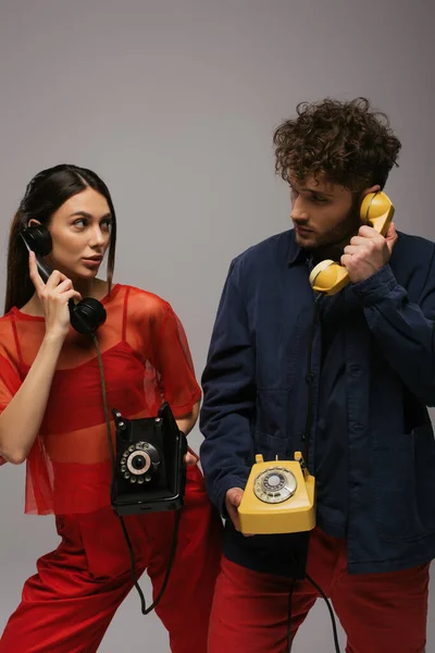 Trendige Frau und lockiger Mann mit Retro-Handys und Telefonen isoliert auf grau — Stockfoto