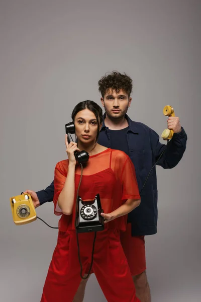 Young woman and curly man holding retro handsets and telephones isolated on grey — Stock Photo