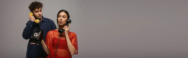 Young woman and curly man holding retro handsets while talking isolated on grey, banner — Stock Photo