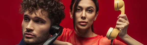 Young woman and curly man holding retro handsets while posing on red, banner — Stock Photo