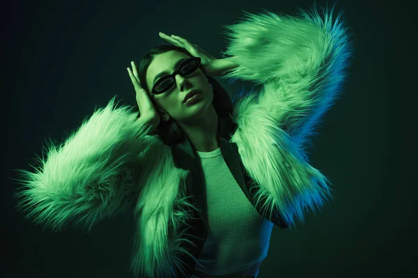 Elegante giovane donna in pelliccia sintetica giacca e occhiali da sole in posa su blu — Foto stock