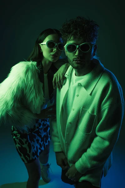 Uomo e donna alla moda in occhiali da sole e abiti alla moda in posa su blu scuro — Foto stock