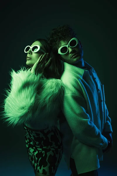 Modelos elegantes jovens em óculos de sol e roupas da moda posando em azul escuro — Fotografia de Stock