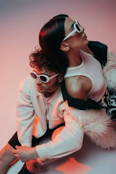 High angle view of stylish man in sunglasses and woman in faux fur jacket sitting on pink and grey — Fotografia de Stock